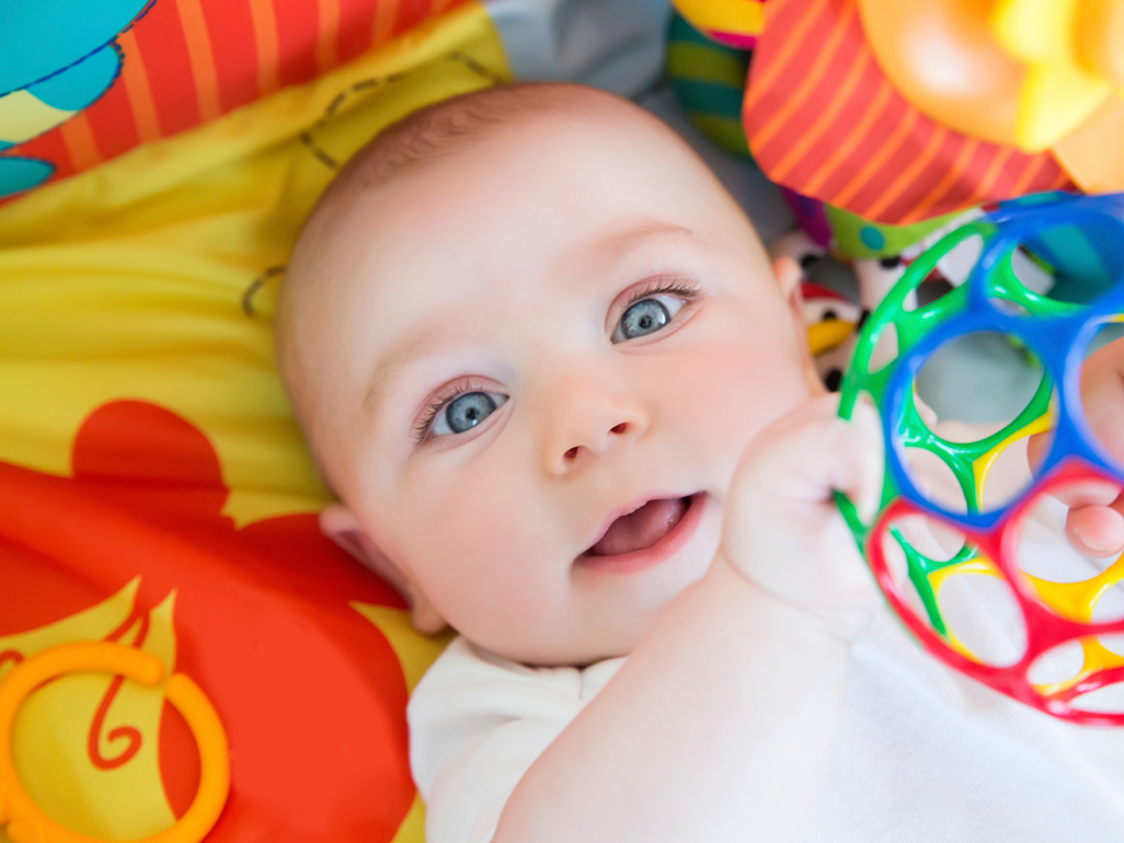 baby holding onto toy hanging from play mobile