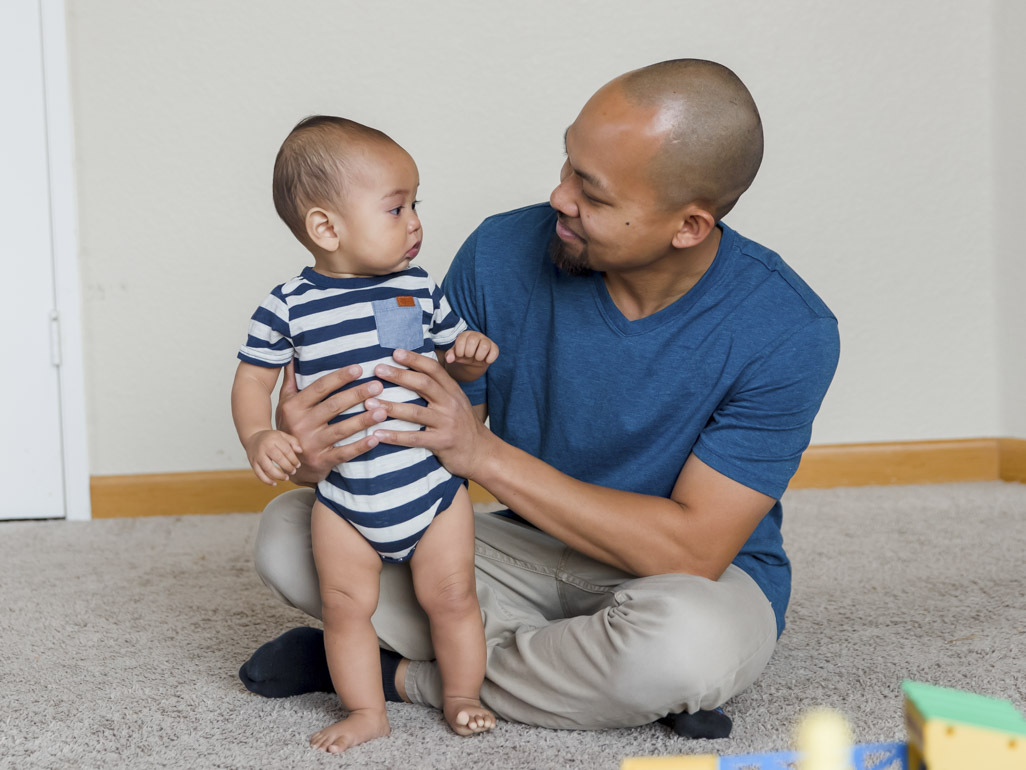 Baby standing with dad's help and looking at him