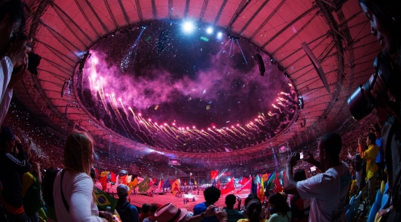 A crowded sports stadium, lit by fireworks at the opening ceremony of the Olympic games 