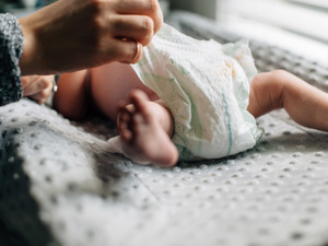 A close-up of a woman's hand changing a newborn baby's diaper.