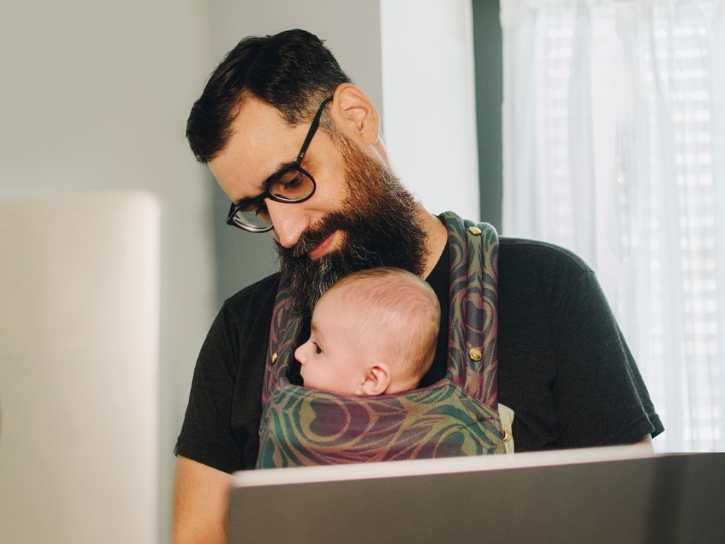 Dad working at a laptop with a baby in a front carrier