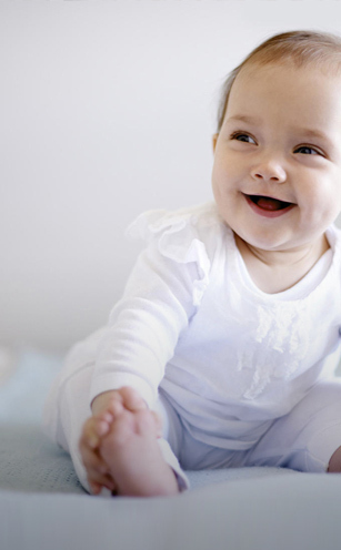 A smiling baby sits upright on a blue blanket