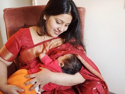 woman sitting in an armchair and breastfeeding her baby