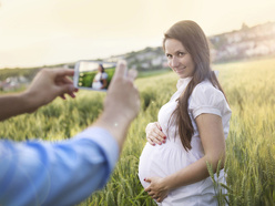 pregnant woman posing in field while man takes photo with phone