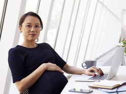 pregnant woman leaning back in her desk chair, in front of a laptop