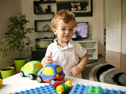 18-month-old boy standing at a table and playing with toy cars