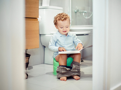 toddler boy sitting on a green potty in the bathroom and looking through a book