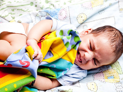 Upset baby in bed with a multi-coloured blanket.