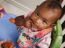 Baby in a high chair eating a spoonful of puree