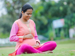 Smiling pregnant woman sitting cross-legged on the ground, holding her baby bump