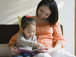 woman sitting next to small child reading a book together