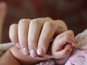 A person with a cross tattoo on their finger holding a newborn's hand