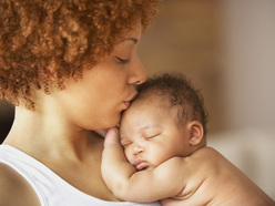 A person kissing the forehead of a sleeping baby