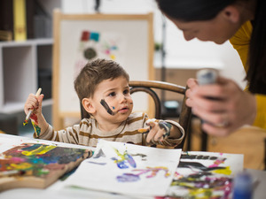 young child making a mess painting while looking at adult