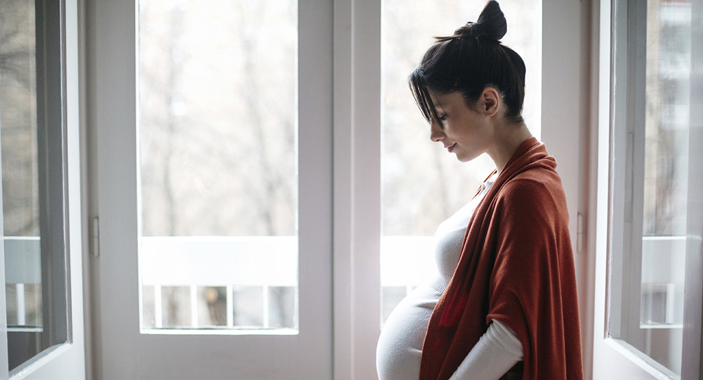 side view of a pregnant woman looking down at her pregnant stomach