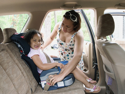 woman buckling laughing child into booster seat with lap-sash seatbelt