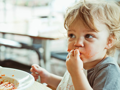 toddler using his fingers to feed himself pasta from a bowl