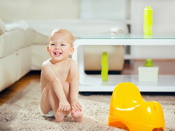 grinning toddler sitting on the floor next to his yellow potty