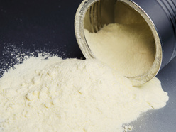 tin lying on its side on a grey bench, with formula milk powder spilling out