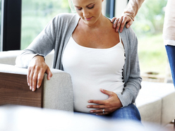 a pregnant woman sitting and holding her belly, with a friend beside her