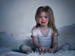 Little girl sitting up and crying in bed