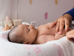 Woman's hands on the bare chest of a newborn baby