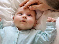 Adult hand gently stroking sick baby's forehead as baby looks up