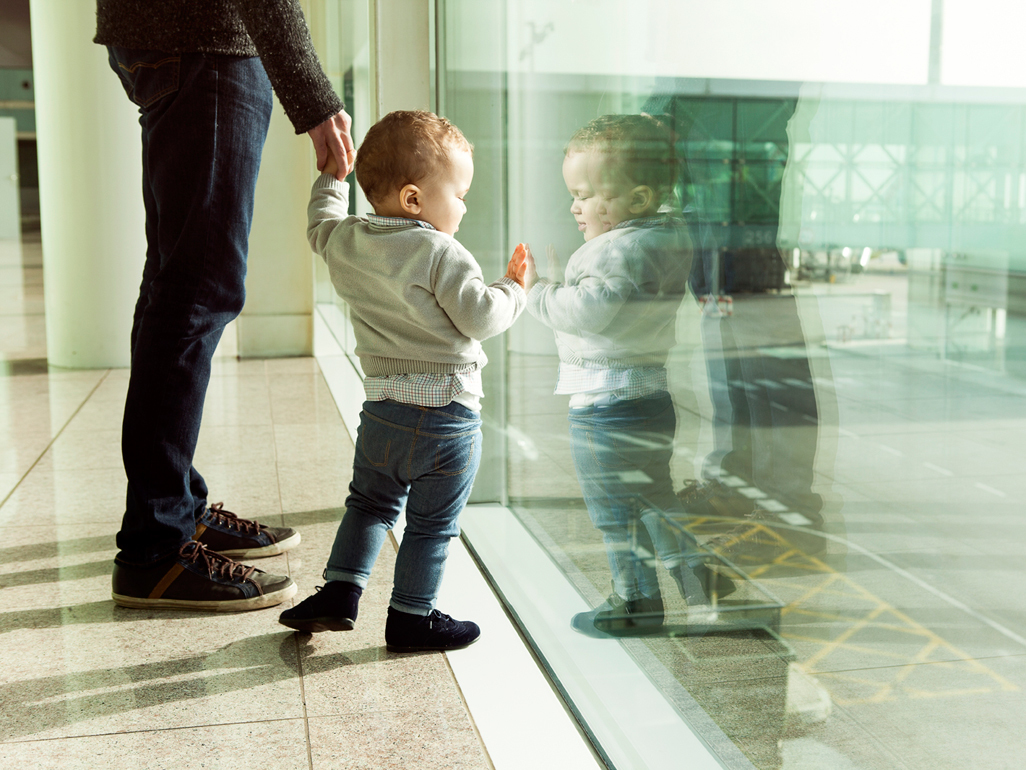 A person holding a toddler's hand while they look out an airport window