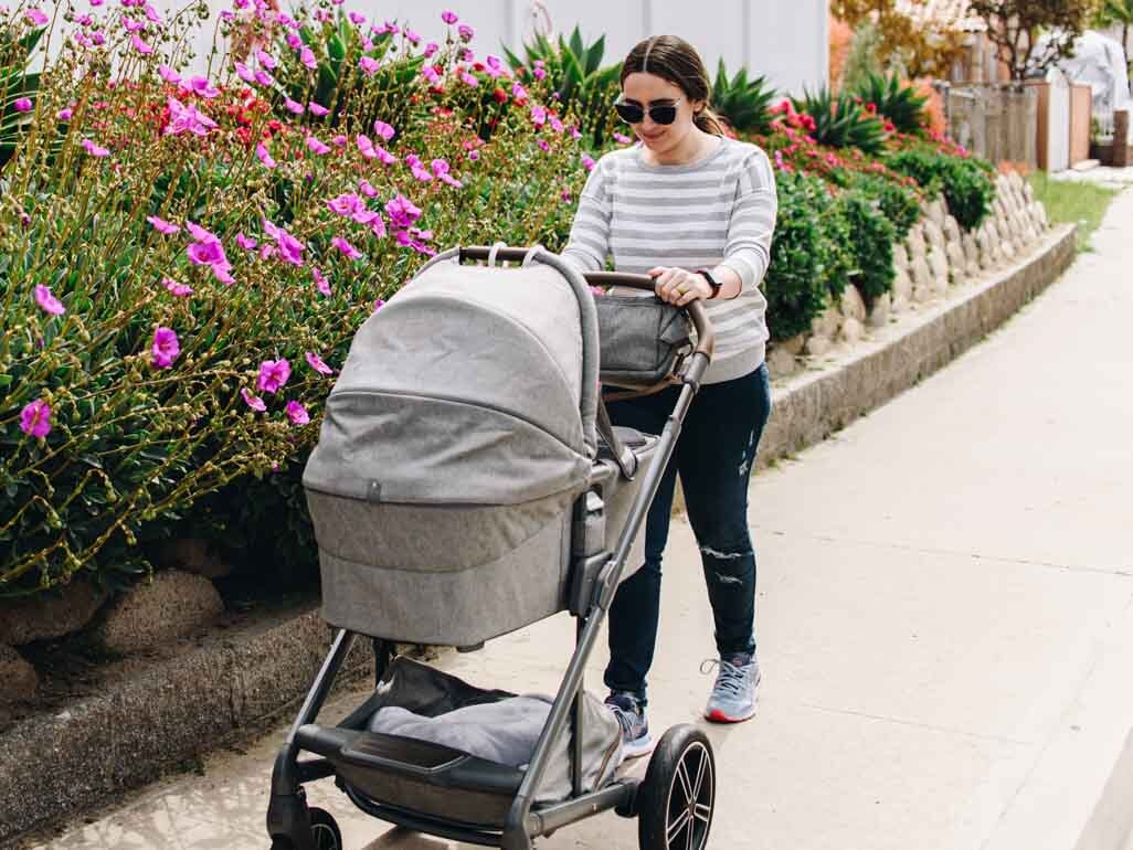 A woman pushing her baby in a stroller with the text "babycenter answers, When can I take my newborn outside?"