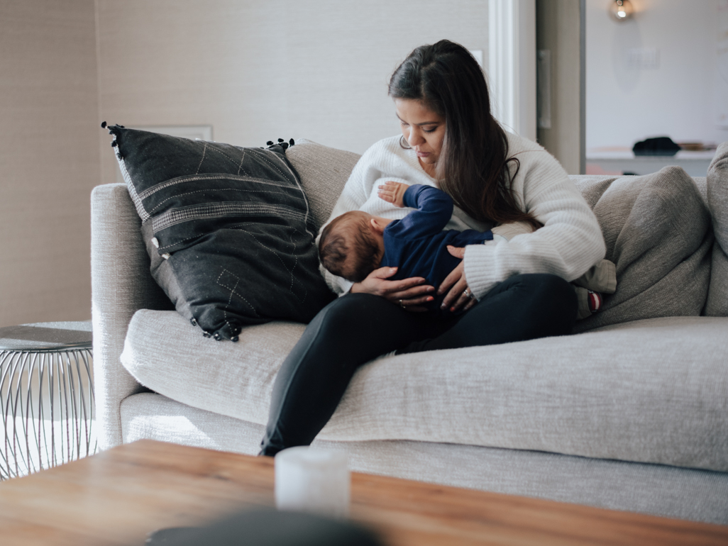 A mom sitting on a couch and breastfeeding her baby.