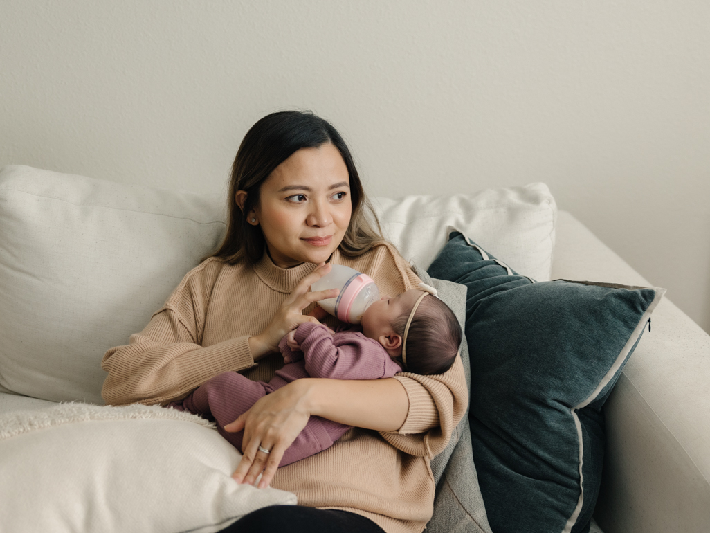 A mom sitting on a couch, bottle feeding her newborn baby.