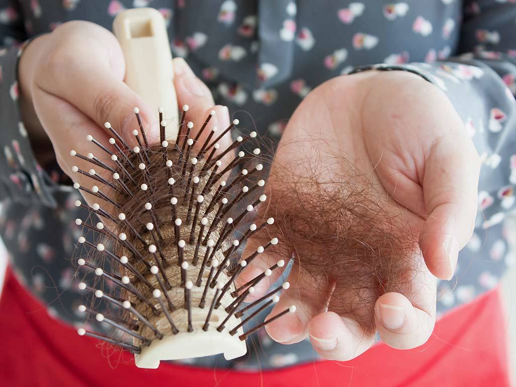 Woman looking at hair on hairbrush and touching head.