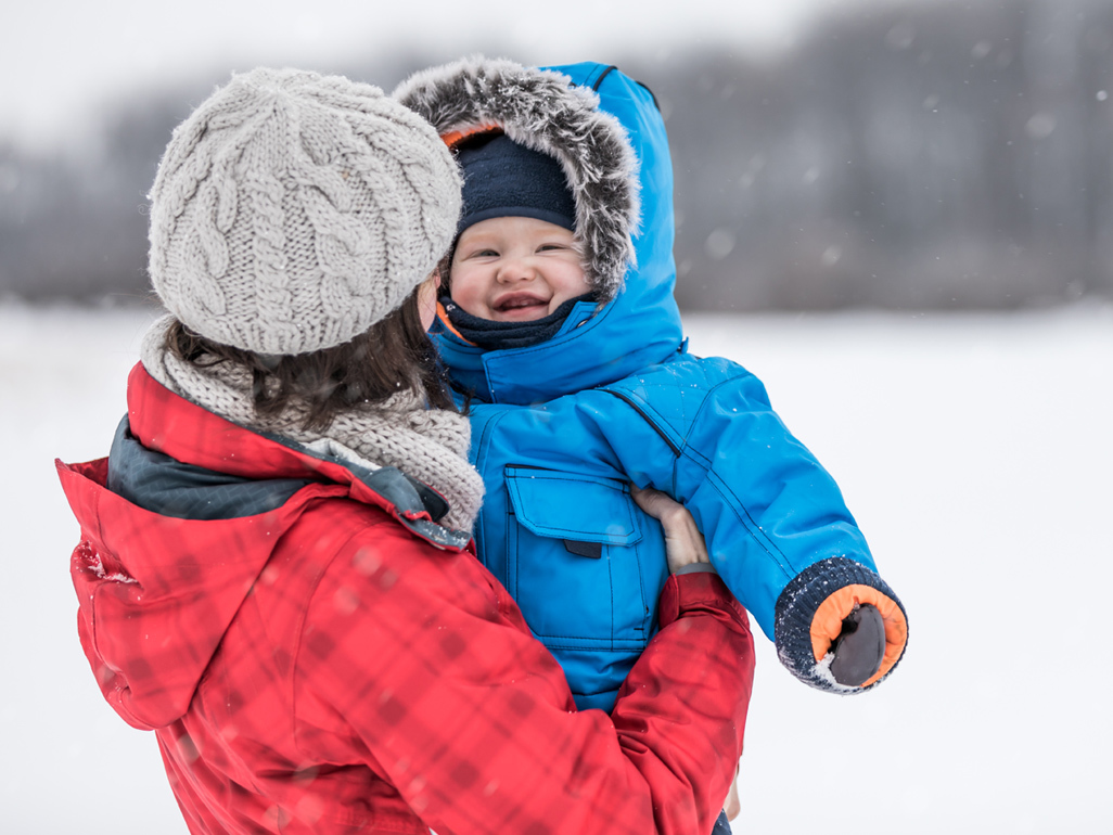 baby being held outside wearing winter clothing among the snow