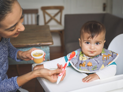 Baby in highchair looking at the camera and being fed with a spoon