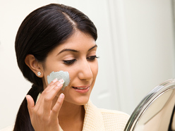 woman putting on face cream while looking at herself in a mirror