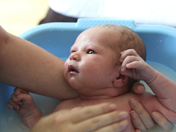 Newborn in bath tub looking up at mum