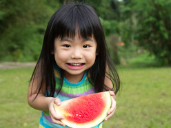 smiling little girl eating a watermelon outdoors