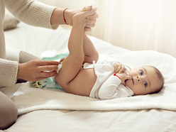 Baby lying on a bed while her mother changes her diaper