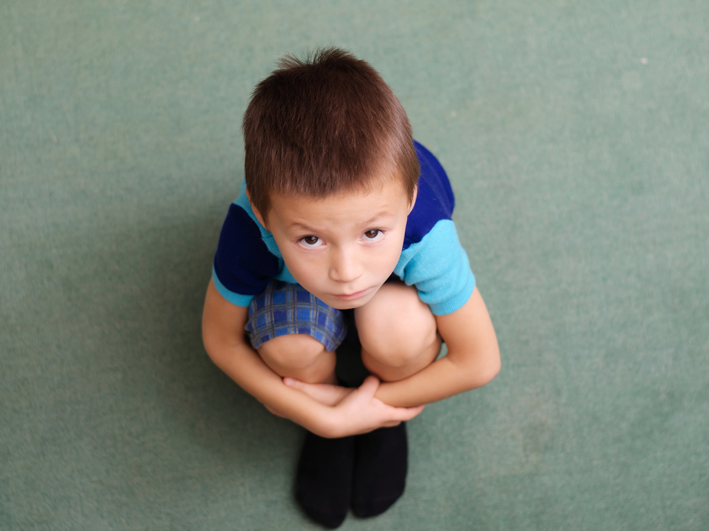 boy sitting on the ground looking sad and holding his knees