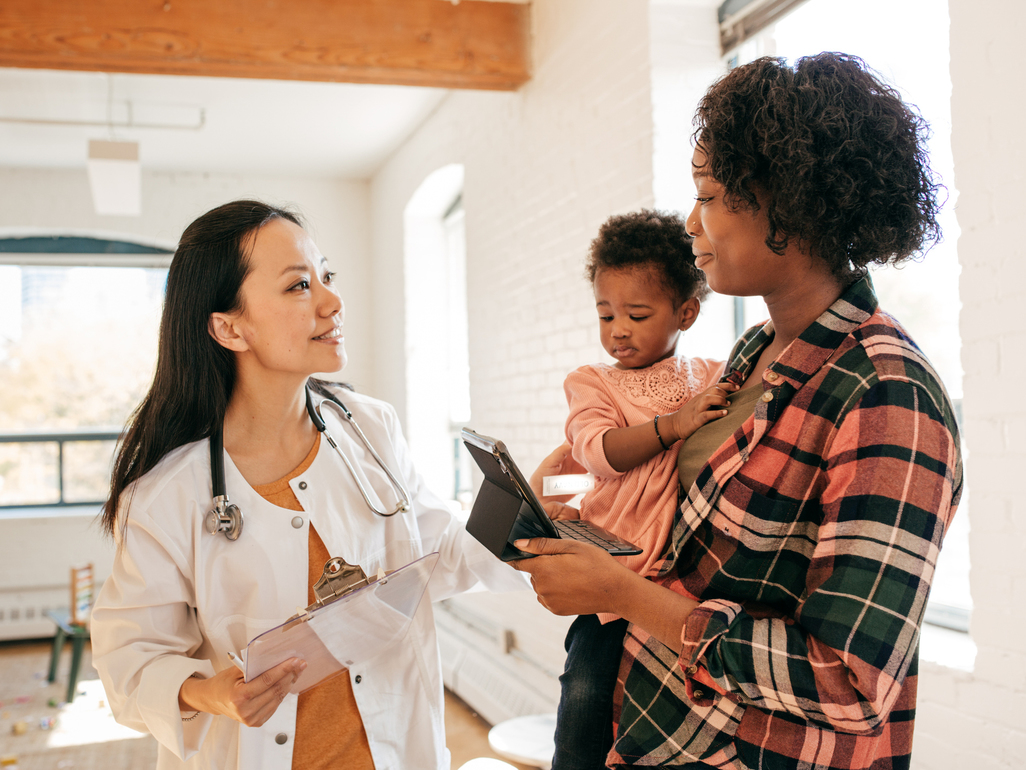 little girl in mother's arms looking sad in front of a doctor