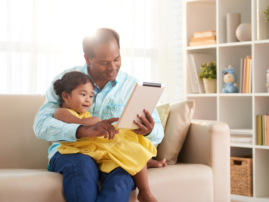 father showing his daughter a tablet while sitting on the couch