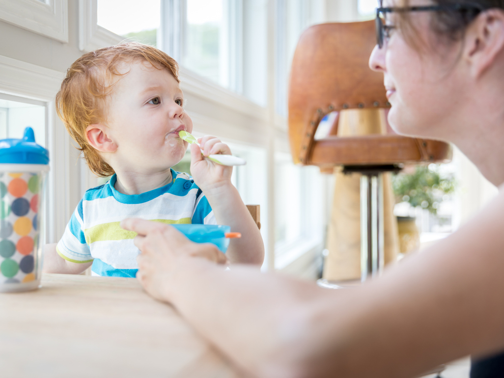 boy sitting at a table and eating while his mom helps him