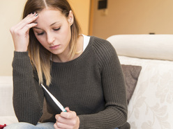 Woman sitting on sofa holding negative pregnancy test