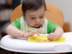 Baby picking up finger foods from a plate.