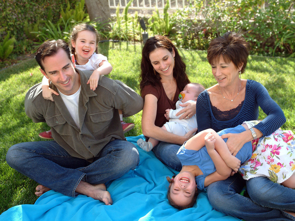 parents with school-age girl, toddler and baby sitting and laughing outside with grandma