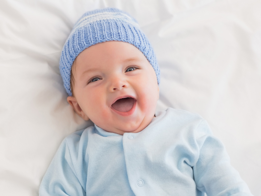 Smiling baby in a blue wooly hat.