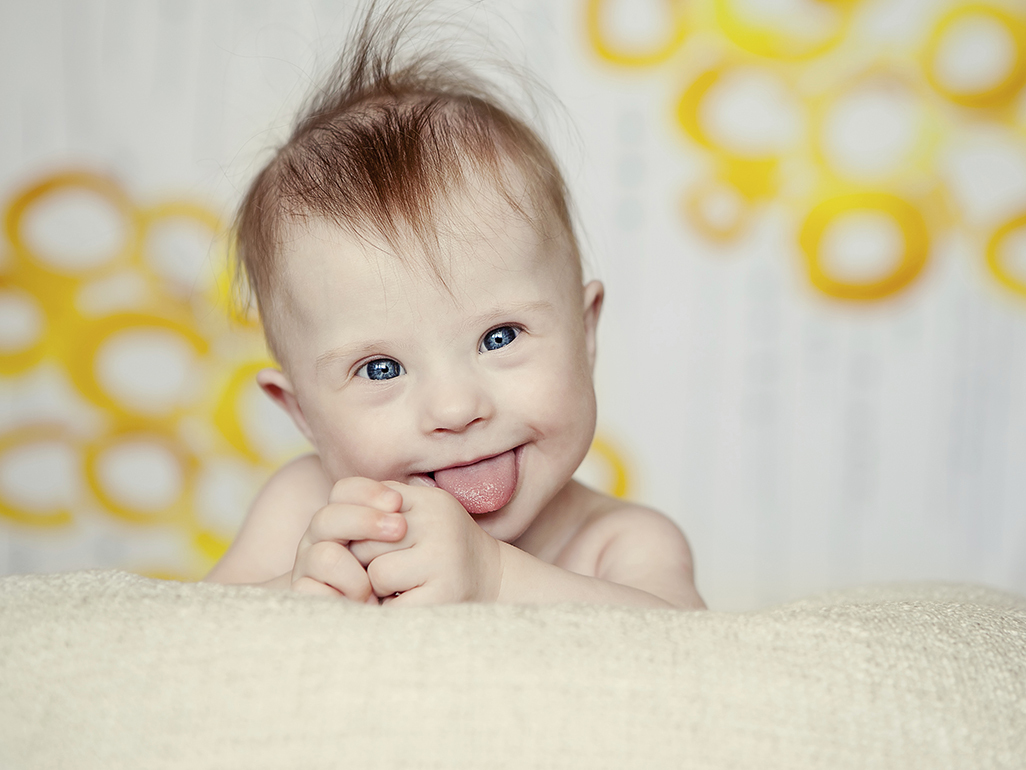 smiling baby looking over back of couch, in front of curtains with big yellow swirls