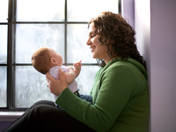 Mutter sitzt in einer Fensternische und betrachtet Ihr junges Baby