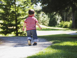 Back of little boy walking along path in park