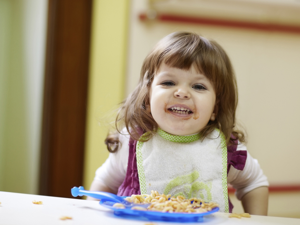 smiling toddler girl with a blue plate full of pasta